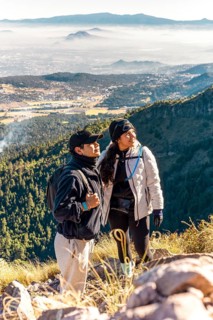 Two friends stand on a mountain overlooking a vast valley, enjoying the scenic view Dressed in