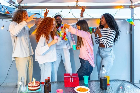 Happy multiracial group of friends dancing celebrating birthday party at terrace
