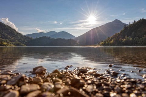Peaceful lake with mountain backdrop, golden sky and sunlight on water and stones, Weitsee