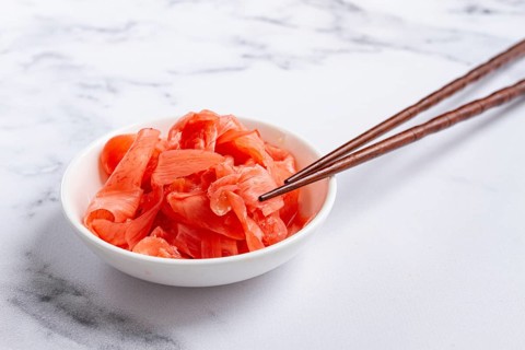 Pickled ginger, with chopsticks, in a small white bowl, on a marble countertop, close-up, no people