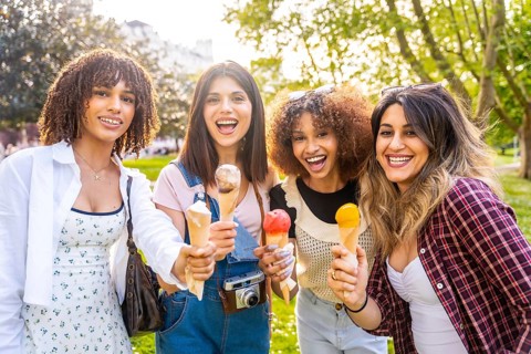 Four smiling, multi ethnic women enjoying ice cream cones while relaxing in a park on a sunny