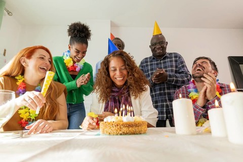 A joyful group of friends gathers to celebrate a birthday. They are all smiling and wearing party