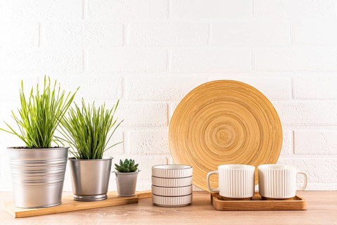 A contemporary kitchen setting featuring a wooden round plate, white striped mugs on a tray, and