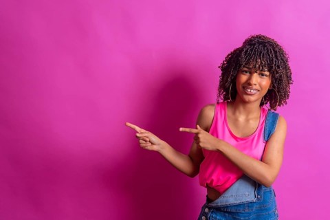 Young woman indicating empty space on a vibrant pink background, ideal for showcasing products or