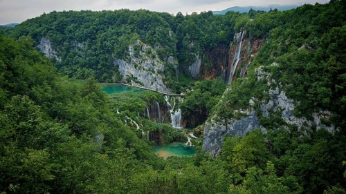 A dramatic waterfall flows through a dense green forest nestled in rock formations, Plitvice Lakes