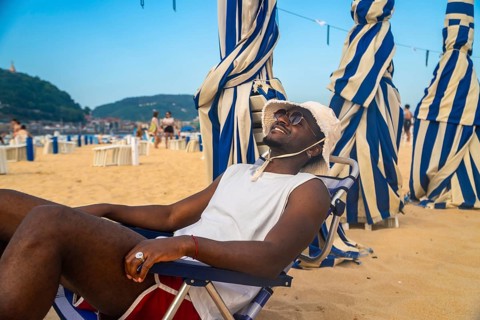 Young black man relaxing in a beach chair, smiling with sunglasses and a bucket hat, enjoying the