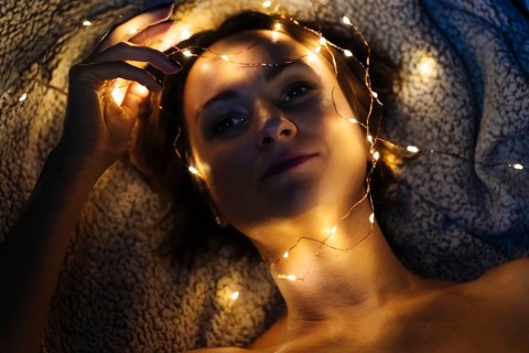 Close-up of woman's face with festive lights. Woman lies on textured blanket with warm yellow fairy