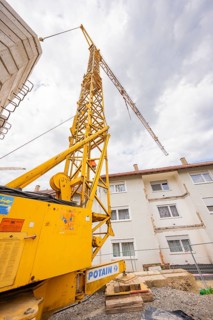 Yellow crane on a construction site in front of a faulty apartment building with clouds in the sky,