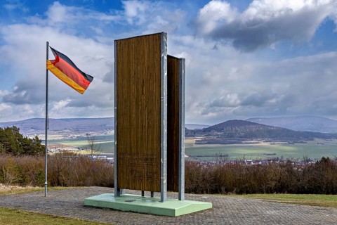 Wooden monument and German flag with a view of a hilly landscape under cloudy sky, the Point Alpha