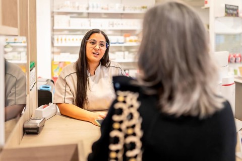 Woman and pharmacist talking in the counter of a modern pharmacy store full of products