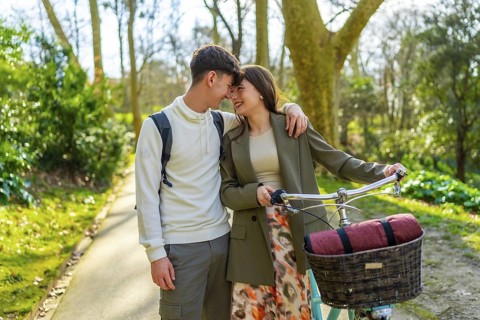 Romantic couple enjoying a leisurely springtime bike ride in a park, embracing and smiling