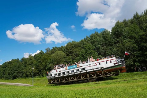 Boat with passengers on a railway carriage in front of a wooded backdrop in good weather, ship