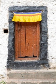 A rustic wooden door adorned with a vibrant yellow, red, and blue fabric in the Zanskar Valley,