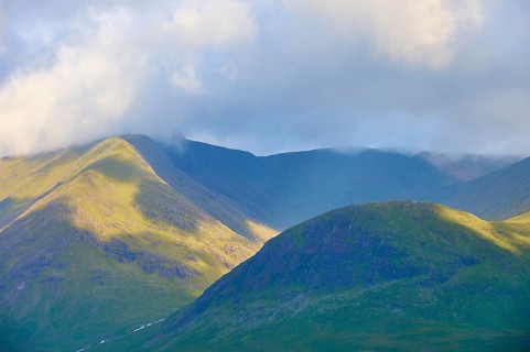 Sunlight illuminates mountainous landscape surrounded by clouds, Rannoch Moor, Bridge of Orchy,