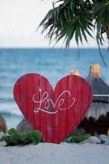 A vibrant red heart with Love inscribed, set against the serene backdrop of Tulum's beach in
