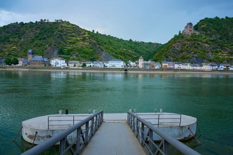 Boat dock on a river with a view of a village and Katz Castle on a hill, St. Goarhausen, Rhine,