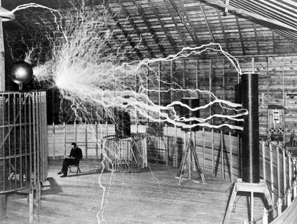Nikola Tesla sits next to his amplifier transmitter, which could generate millions of volts.