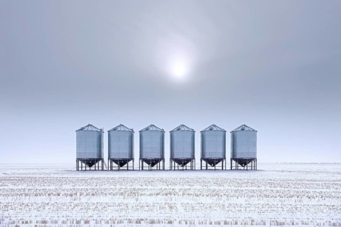 Row of grain bins, stainless steel silos for bulk storage in snow covered field at Saskatchewan in