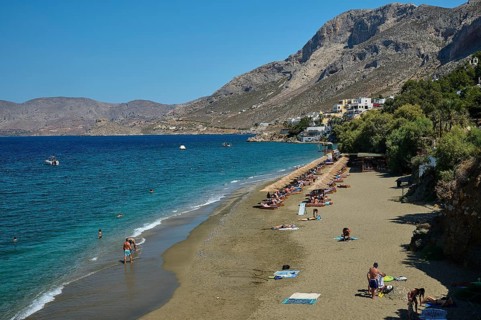 Massouri, people relaxing on sandy beach with mountains in the background and swimming in the clear