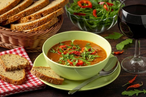 Goulash decorated with paprika and arugula, served with bread, salad and red wine