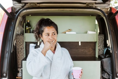 A woman brushes her teeth outside her van while enjoying an autumn morning in New Zealand. The