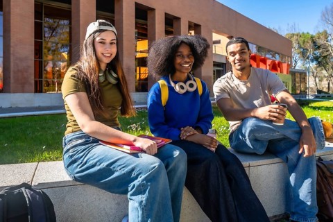 Diverse young students relaxing together on a university campus wall, smiling at the camera and
