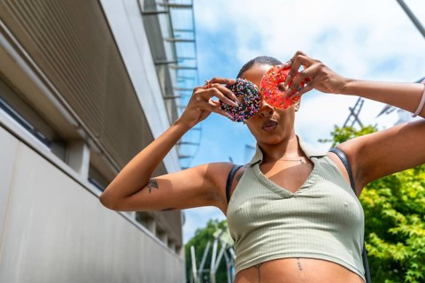 Young woman holding two brightly colored donuts with sprinkles over her eyes, playfully acting like