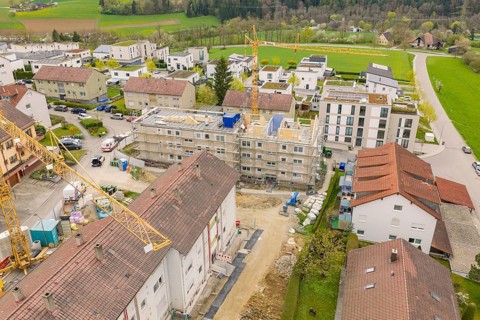 Aerial view of construction site in residential area with surrounding buildings and landscape,
