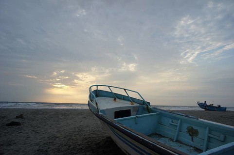 Old fishing boat on an empty beach with a quiet sea scene in the background of the setting sun,