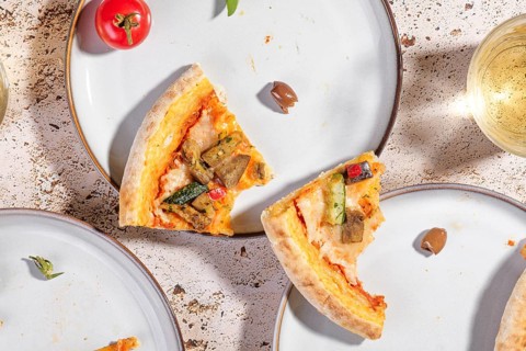 Overhead view of vegetarian pizza slices on a white plate featuring zucchini, eggplant, and bell