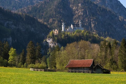 A hut stands in a meadow in picturesque natural surroundings, with an impressive castle in the
