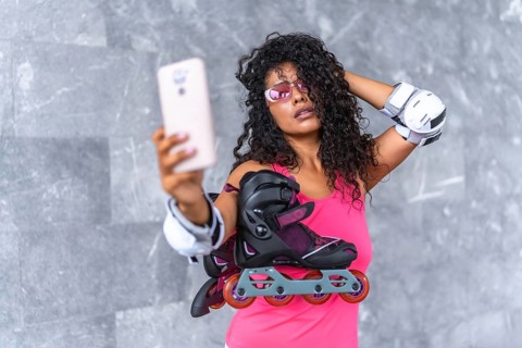 Sensual latin female skater in pink sportive clothes, sunglasses and protective gear taking selfie