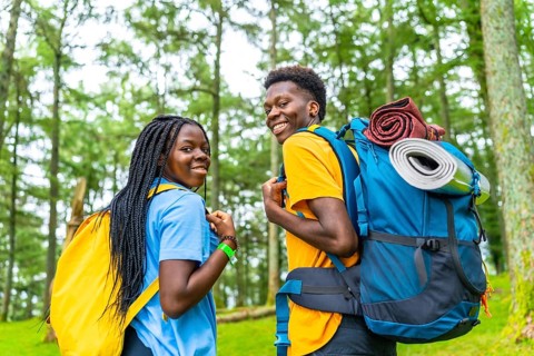 Rear view of african friends turning to smile at camera while walking along green forest
