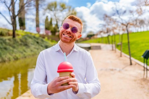 Young redhead man with sunglasses and white shirt holding a beverage with straw and red lid,