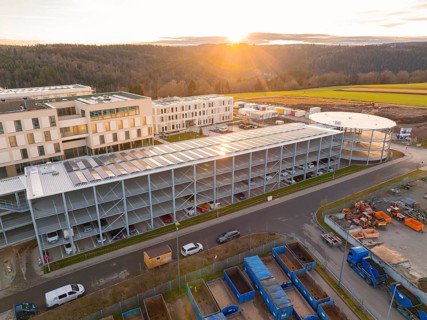 Industrial complex with multi-storey car park and modern buildings, at sunset, in a rural setting,