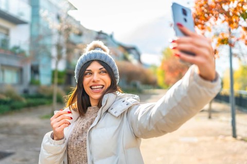 Happy beauty woman smiling at camera while taking selfie with smartphone standing in the street in