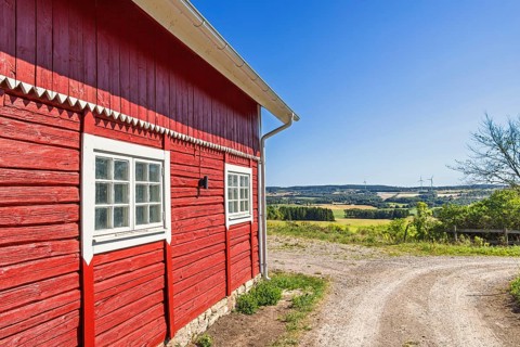 Red wooden barn with white trim stands beside a curved dirt road in a scenic rural landscape with
