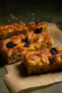 Close up of freshly baked homemade focaccia bread, topped with rosemary and black olives, placed on