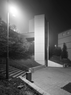 A contemporary urban elevator emerges from the mist in a nocturnal setting, highlighted by ambient