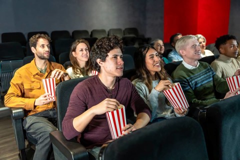 Group of diverse friends enjoying a movie at the cinema, eating popcorn and having fun together