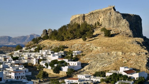 Sunny landscape with ancient fortress on a rock above white buildings, Acropolis of Lindos, Lindos,