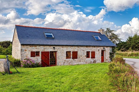 Stone house with red doors in rural surroundings under cloudy sky, surrounded by meadows, historic