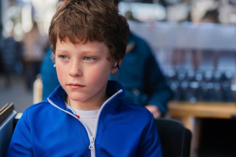 A young boy wearing headphones appears deep in thought while sitting on a tourist bus. His striking