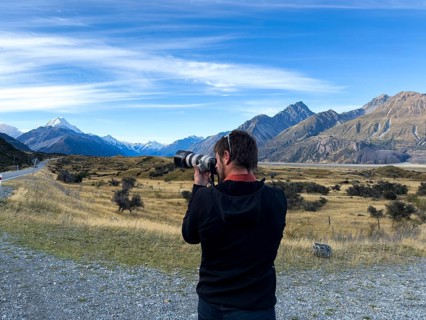 Back view of unrecognizable man capturing the breathtaking landscape of Mount Cook in New Zealand.
