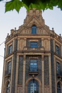 Historic building with rich brick architecture and decorative elements surrounded by green leaves,