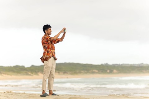 An indonesian man wearing traditional batik clothing captures a scenic moment on an Australian