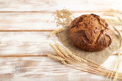 Fresh homemade golden grain bread with ears of wheat and rye on white wooden background and linen