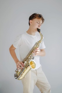 A young boy musician passionately plays the saxophone, eyes closed, dressed in casual attire. The