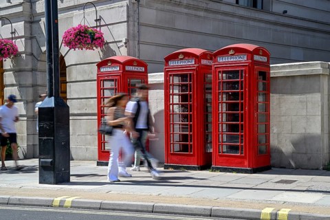 Passers-by in front of three traditional red telephone boxes in Langham Place, City of Westminster,