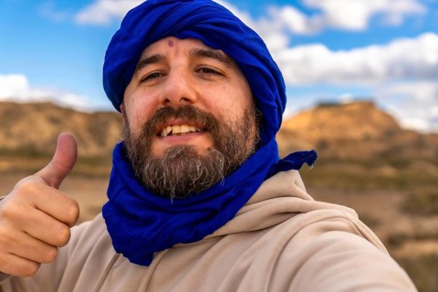 Bearded man wearing blue turban making thumbs up gesture while visiting bardenas reales desert in